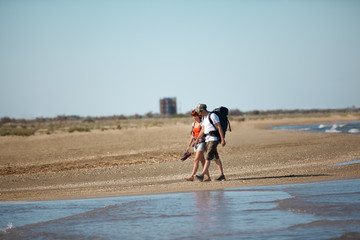 couple with backpacks walking on sea shore