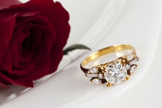 Golden diamond ring and rose on white background