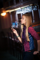 young woman sending sms on smartphone in the interior of the bar