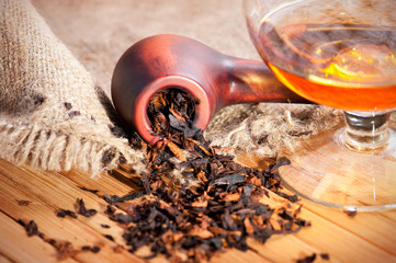 Glass of cognac and pipe with tobacco on wooden table