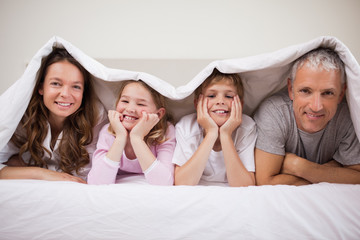 Playful family lying under a duvet