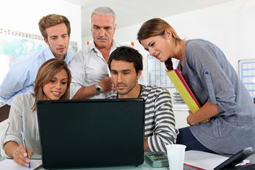 a bunch of people gathered behind a laptop