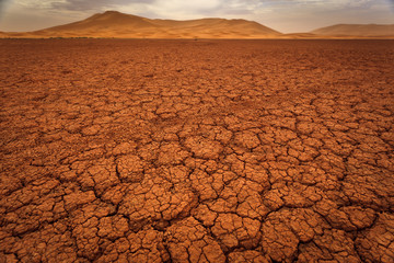 Cracked pattern of dry lake bed and sand dunes in Sahara Desert