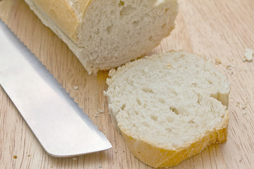 White baguette with slice cut off on wooden board with knife