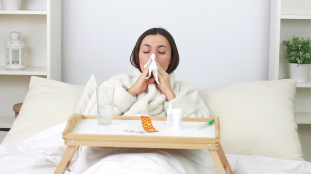 Sick young woman blowing nose and spraying medicine in nostril