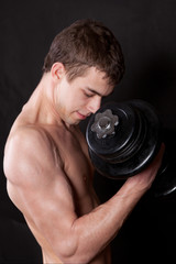 Portrait of  energetic naked man lifting dumbbell on background