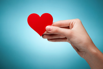 woman's hand holding symbol - red heart. Against blue background