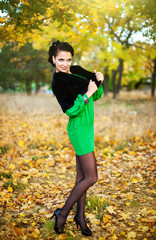 beautiful brunette in a green dress walks on autumn park