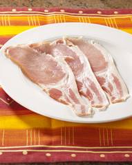Raw bacon slices on a white plate