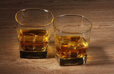 two glasses of scotch whiskey and ice on wooden table