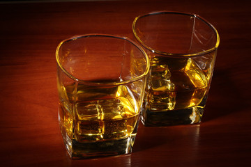 two glasses of scotch whiskey and ice on wooden table