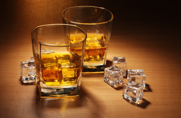 two glasses of scotch whiskey and ice on wooden table