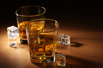 two glasses of scotch whiskey and ice on wooden table