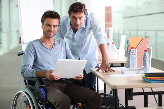 Man in wheelchair holding laptop computer next to colleague