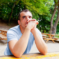 Portrait of thoughtful man with arms on the table; outdoors
