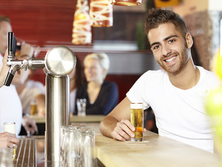 Smiling young man drinking a glass of beer in a pub