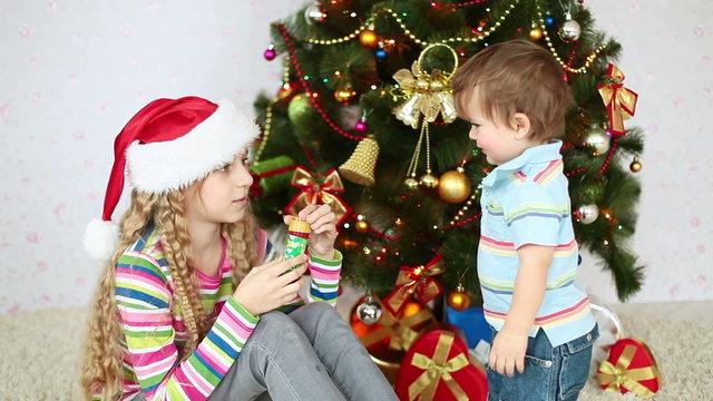 Sister and brother near the Christmas tree blowing bubbles