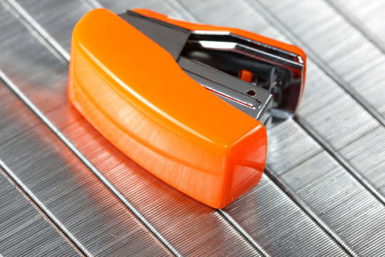 Small orange stapler against staples background