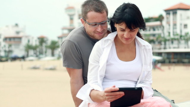 Happy young couple with tablet computer by the beach