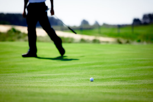 Legs of golfer watching ball roll near hole on green