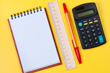 Calculator and notepad on yellow background top view.