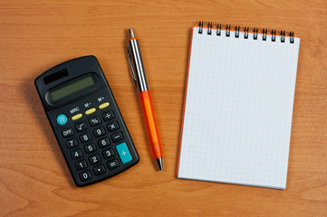 Calculator, notepad and pen on table.