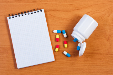 Fototapeta na wymiar Notebpad and pills on table top view.