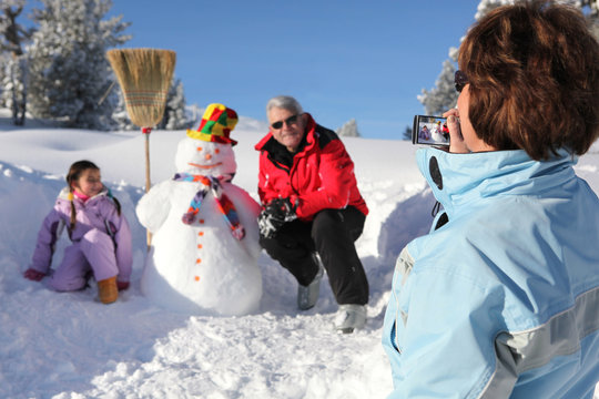 Grandmother taking a picture of her family and their snowman