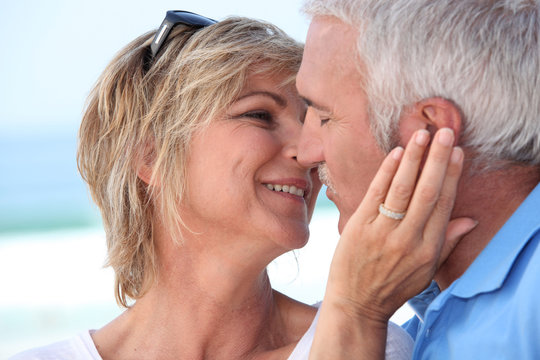Middle aged couple kissing at the beach.