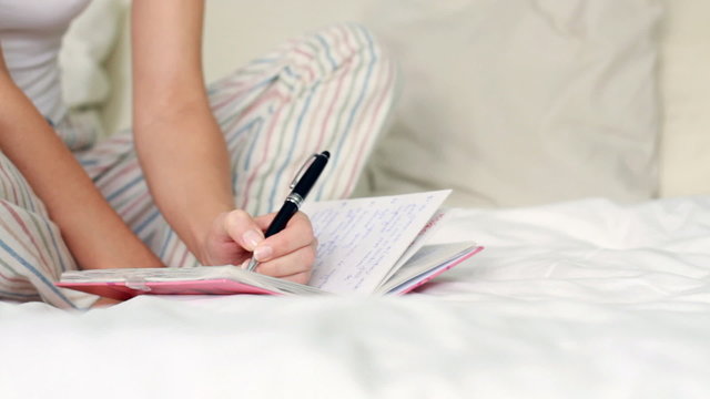 Young woman writing diary while sitting on the bed, dolly shot