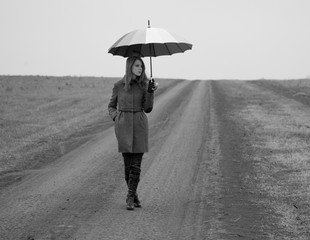 Lonely girl with umbrella at country road.