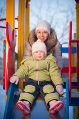 Mother helping baby to slide down on playground