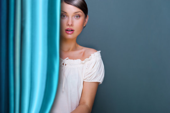 Closeup of young, pretty woman standing near curtain and holding