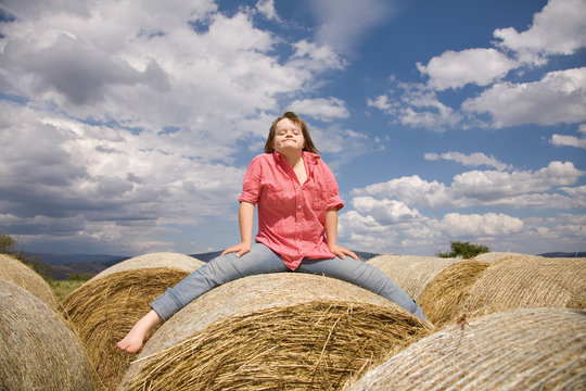 A girl with Down syndrome seated on a straw bale.