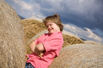 Naklejka na ściany i meble A girl with Down syndrome between straw bales.