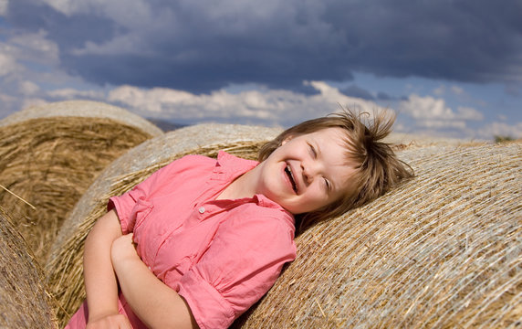 A girl with Down syndrome laughing between straw bales.