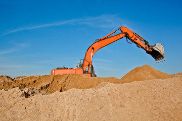 Excavator at a sandpit with raised bucket over sky