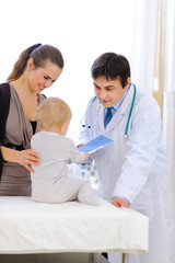 Interested baby holding patients card at pediatricians office