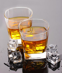 two glasses of scotch whiskey and ice on grey table