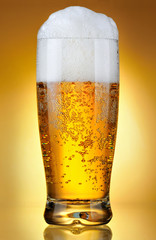glass of beer with froth over yellow background