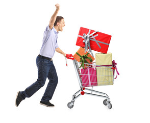 Euphoric male pushing a shopping cart full with gifts