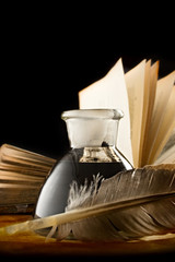 A feather with the bottle full of ink and a book