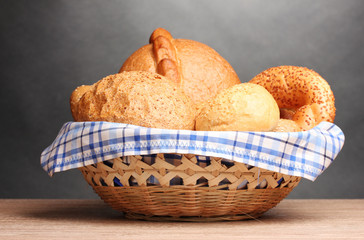 delicious bread in basket on wooden table on gray background