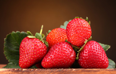 Strawberries with leaves on wooden table on brown  background