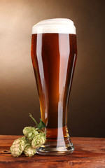 beer in glass and green hop on wooden table on brown background