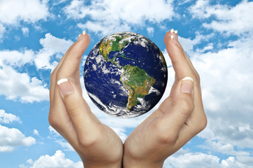 Human hands holding planet Earth against blue sky - Environmenta