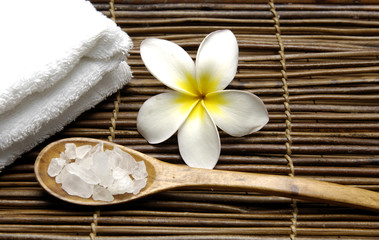 Fototapeta na wymiar Towel with frangipani and salt in spoon on stick straw mat