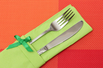 Fork and knife in a green cloth with a bow on a red tablecloth