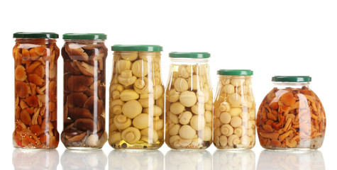 Different glass jars of marinated mushrooms isolated on white