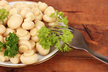 Marinated mushrooms in saucer on wooden table